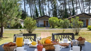 A breakfast table set outdoors with a view of villas, a grassy area, and trees. - Cozy Duplex House With Pool (Sérignan)