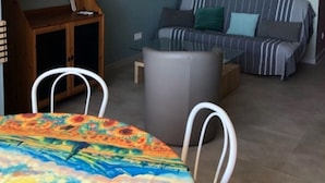 Ett vardagsrum med en soffa, ett matbord med en färgglad duk, ett träskåp och en luftkonditioneringsanläggning.