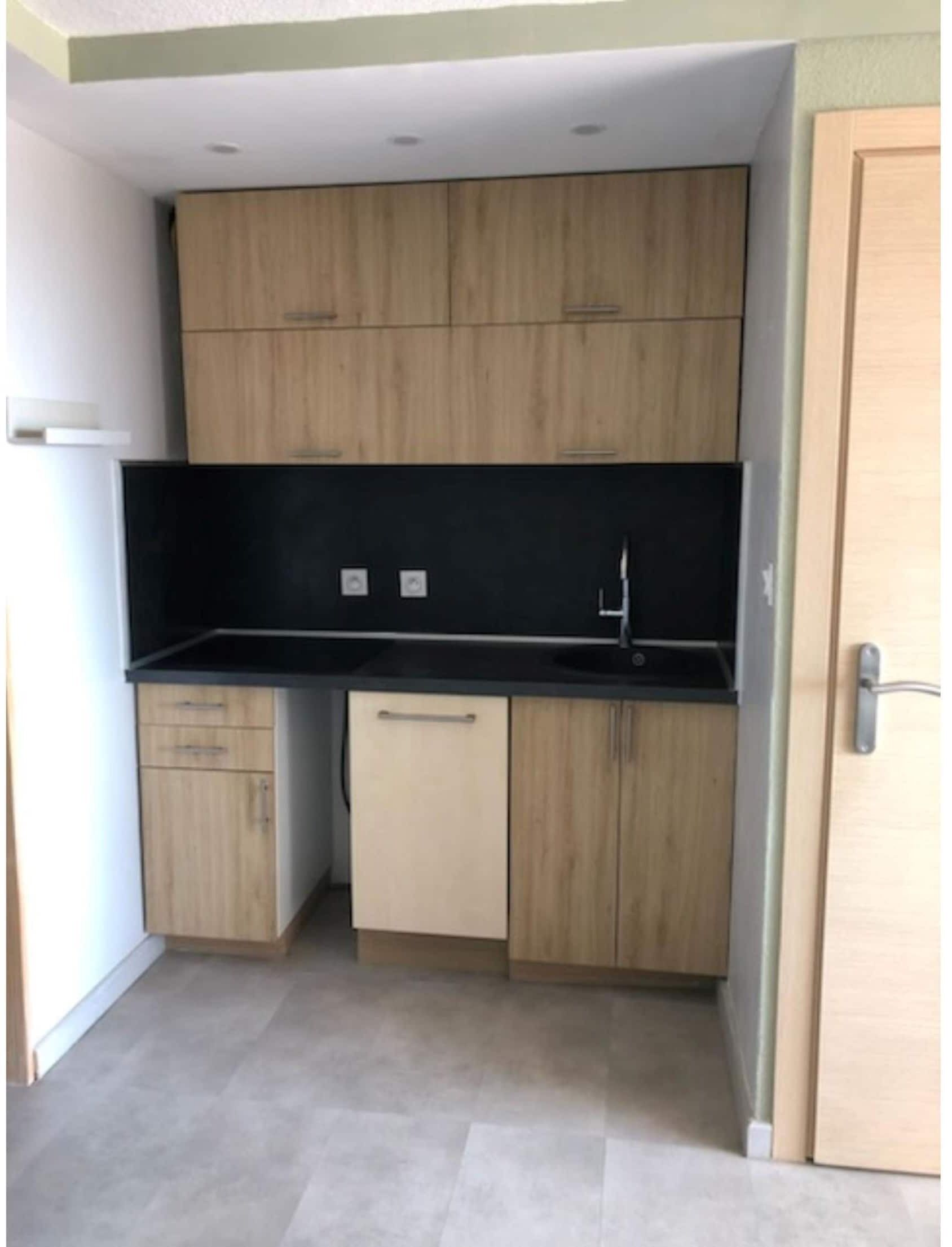 A compact kitchen with wooden cabinets, a black countertop, and a sink.