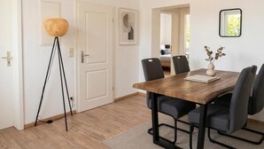 Un comedor con una mesa de madera, sillas negras, una lámpara de pie y un cuadro en la pared.