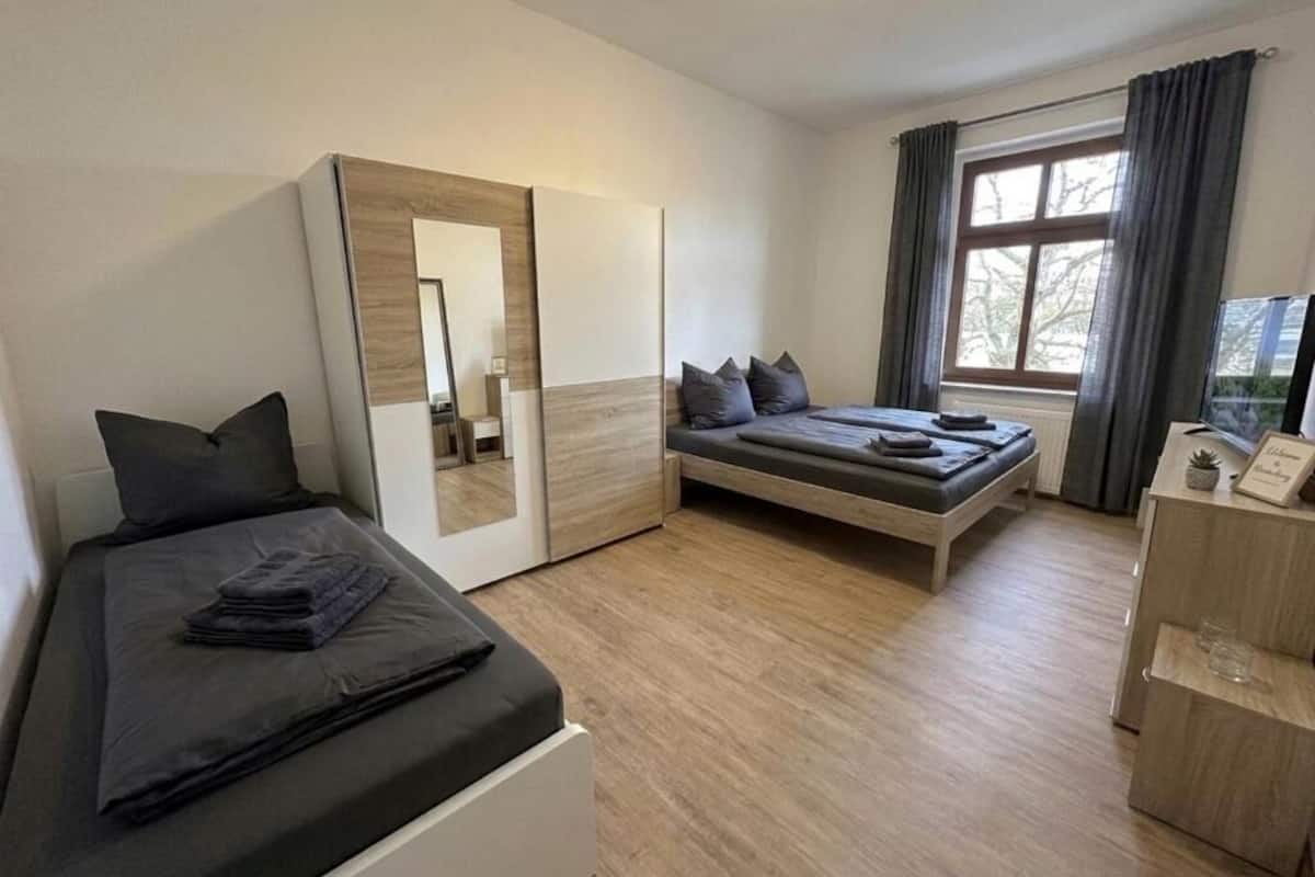 Un dormitorio moderno con una cama, un sofá, un escritorio y una ventana con cortinas.
