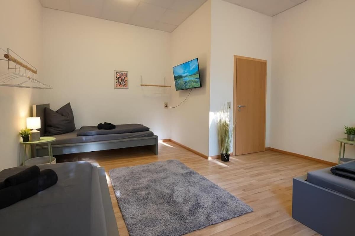 Una sala moderna con un sofá, una mesita con una lámpara, un televisor montado en la pared y una puerta.