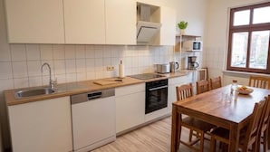 Una cocina moderna con armarios blancos, encimera de madera, horno empotrado y un comedor con sillas y mesa de madera.