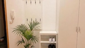 Una habitación con piso de madera, un armario blanco, un zapatero y una planta en maceta.