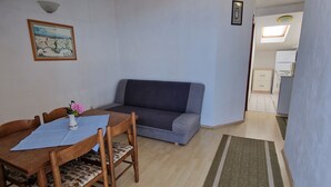 Una habitación con una mesa de comedor, sillas, un sofá, una alfombra pequeña, una lámpara en el techo y un cuadro en la pared.
