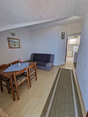 A room with a dining table, chairs, a sofa, a small rug, a ceiling light, and a framed picture on the wall. - Beautiful 2-bedroom apartment with AC in welcoming Gradac (Gradac)
