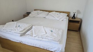 Una cama bien tendida con sábanas y almohadas blancas, una mesita de noche con lámpara y una mesita auxiliar de madera.