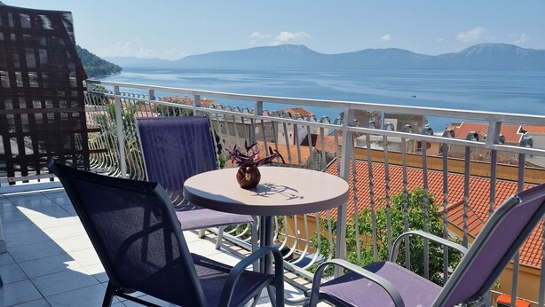Un balcón con una mesa y sillas, una planta en maceta y vistas al mar y las montañas.