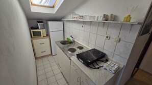 Cocina compacta con microondas, estufa, pileta y heladera pequeña. Hay un estante con utensilios de cocina y una ventana sobre la pileta.