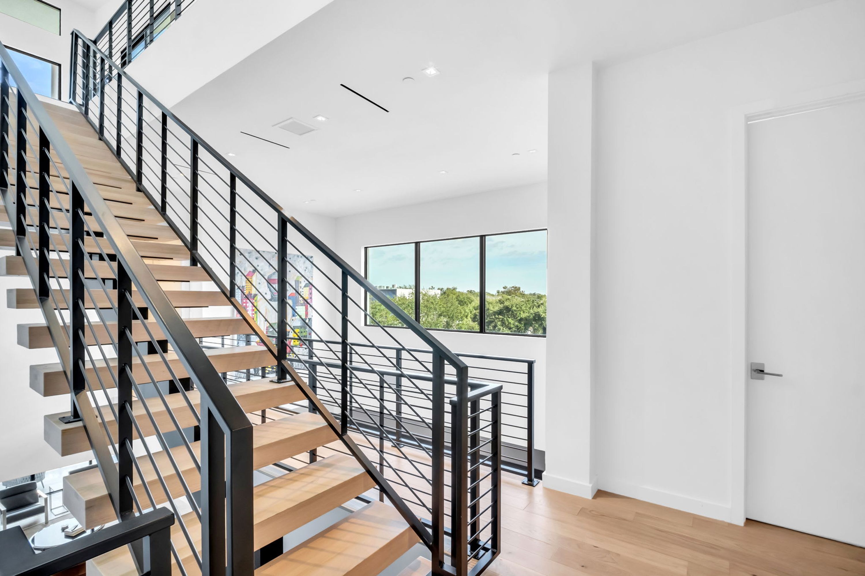 A modern staircase with wooden steps and black railings, leading to a room with a large window and a white door.