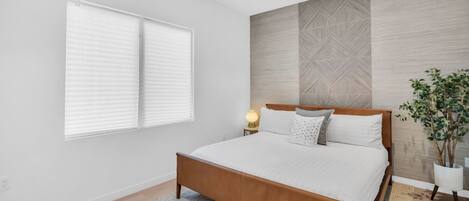Une chambre à coucher avec un lit en bois, une literie blanche, une table de chevet avec une lampe, une plante en pot et une fenêtre avec des stores.