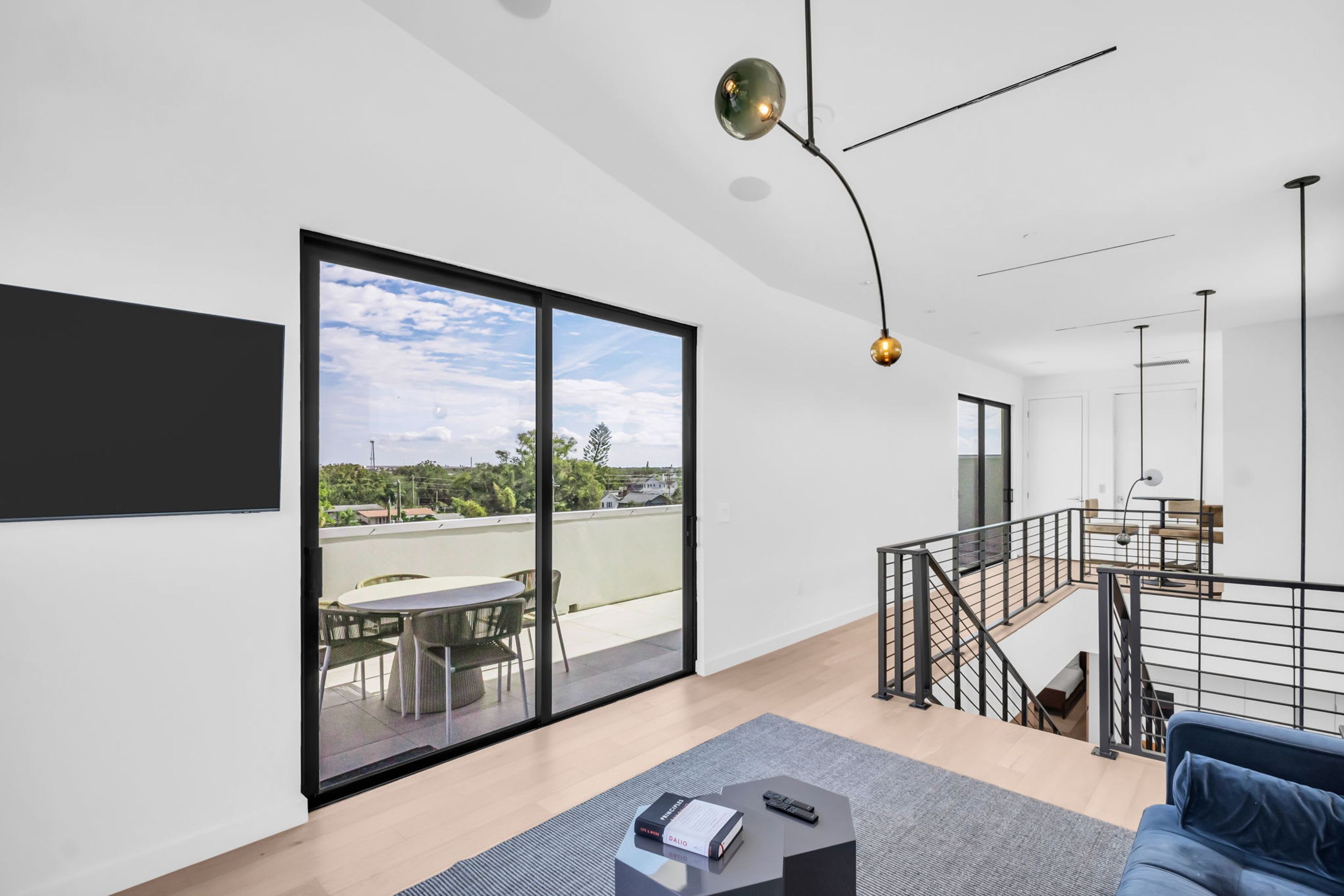 A modern living room with a large sliding glass door, a sofa, a coffee table, and a staircase leading to an upper level.