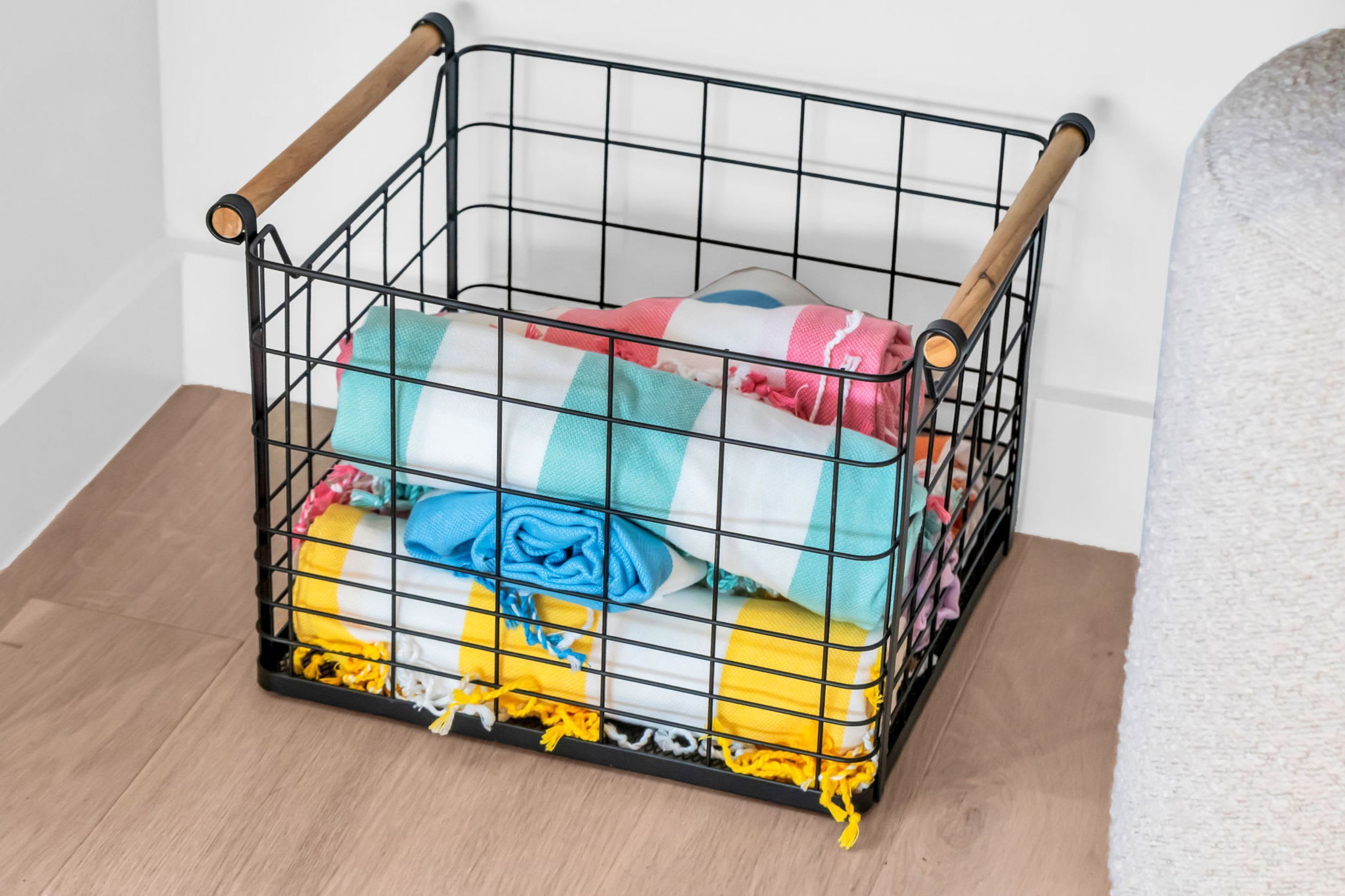 A metal storage bin with wooden handles, containing folded blankets and towels.