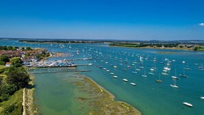 A marina with numerous boats docked, a clear blue sky, and a coastal town in the background. - Stylish Itchenor Home Walk to Harbour Pub (Chichester)