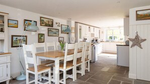 A kitchen with white cabinets, a dining table with chairs, and various framed pictures on the walls. - Stylish Itchenor Home Walk to Harbour Pub (Chichester)