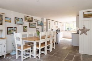 A kitchen with white cabinets, a dining table with chairs, and various framed pictures on the walls. - Stylish Itchenor Home Walk to Harbour Pub (Chichester)
