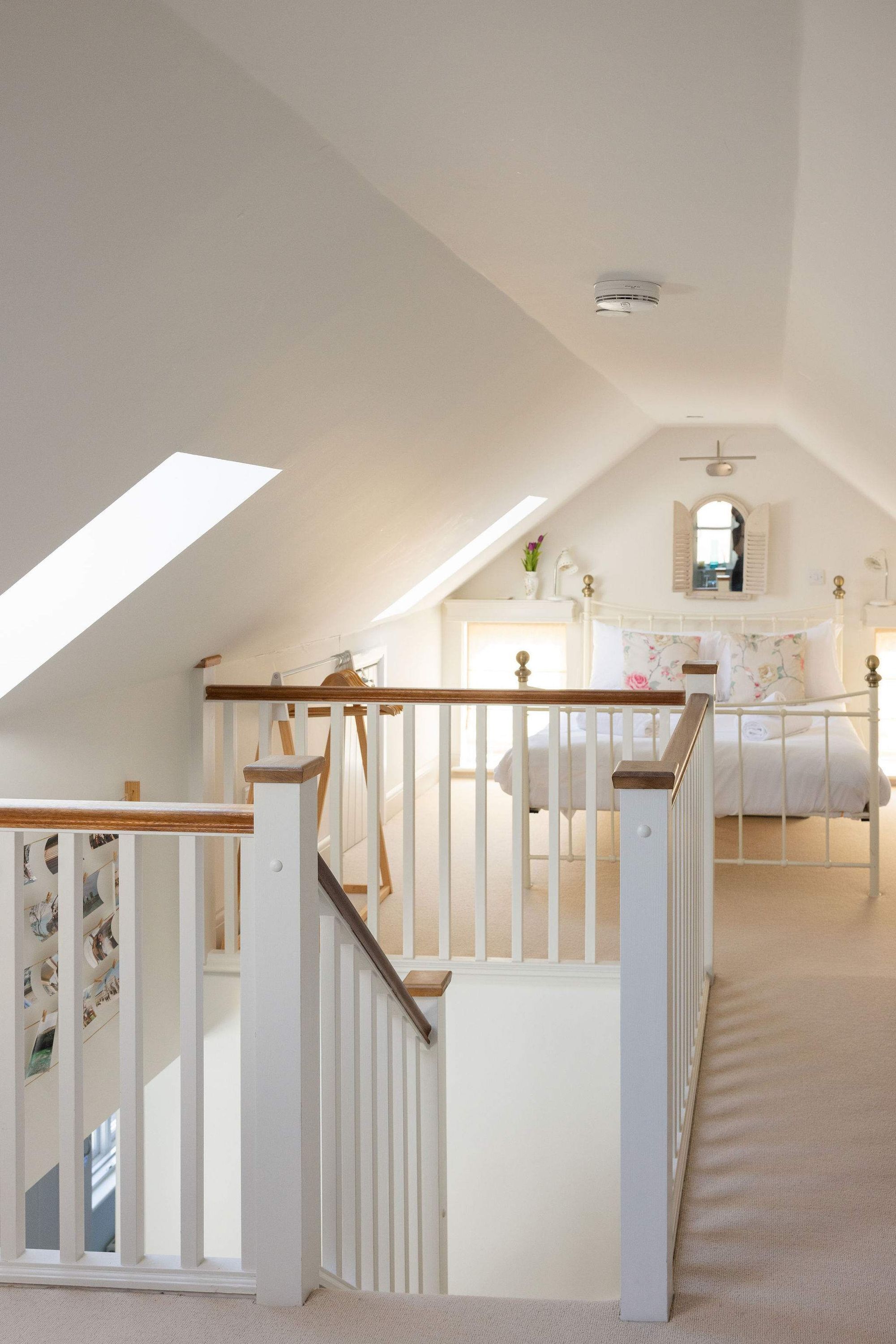 Une chambre avec un plafond en pente, un lit recouvert d’une literie à motifs floraux, une commode blanche et un puits de lumière.