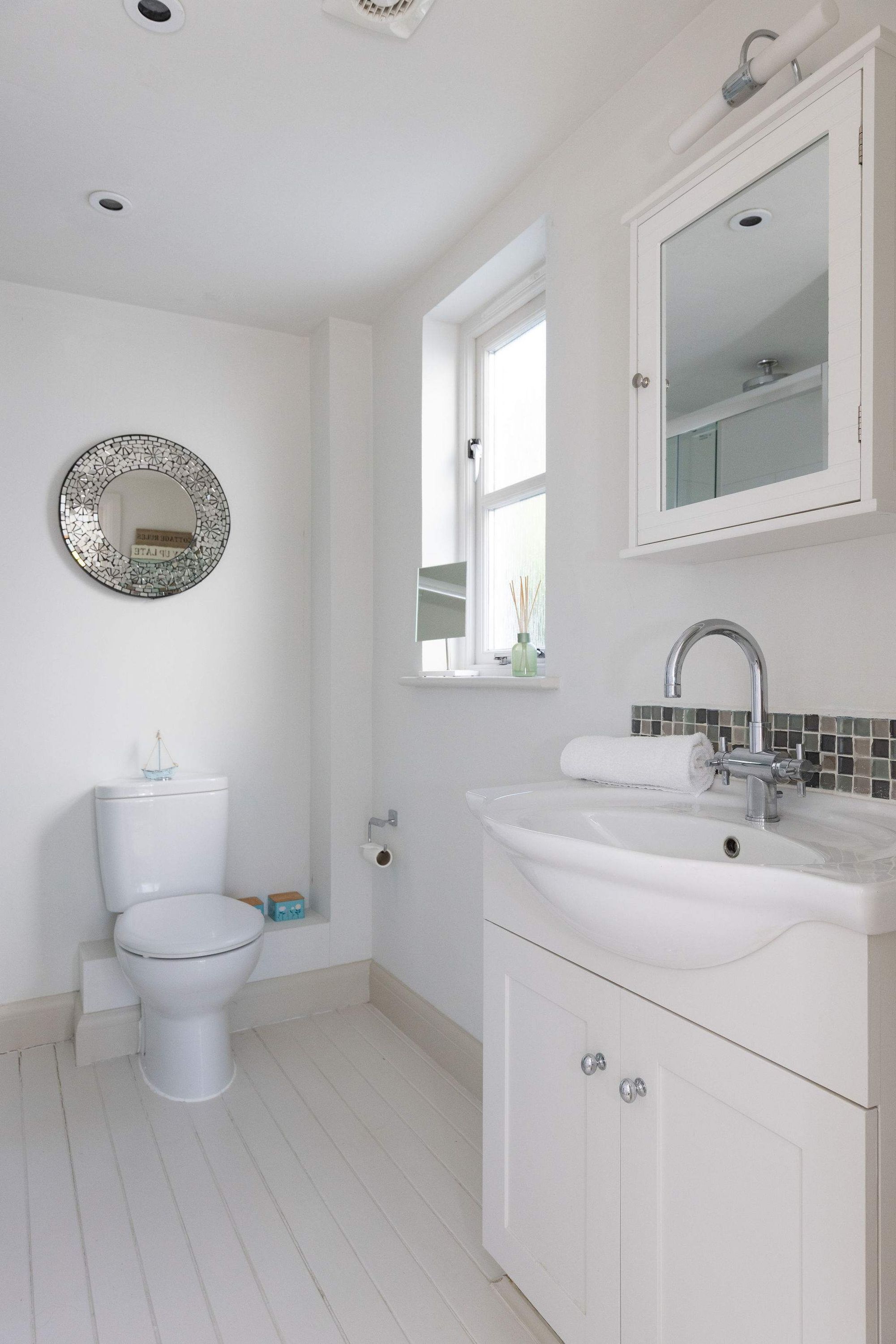 A bathroom with a toilet, sink, mirror, and a window with a view.