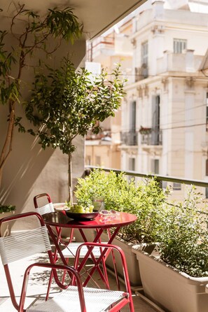 Un balcon avec une table et des chaises, des plantes en pot et une vue sur les bâtiments.