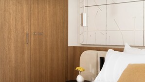Ein Hotelzimmer mit einem Holzschrank, einem Nachttisch mit einer Vase gelber Blumen und einem Bett mit weißen und beigen Kissen.