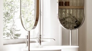 Ein Badezimmer mit einem weißen Waschbecken, einem Spiegel und einem Fenster mit Pflanzen.
