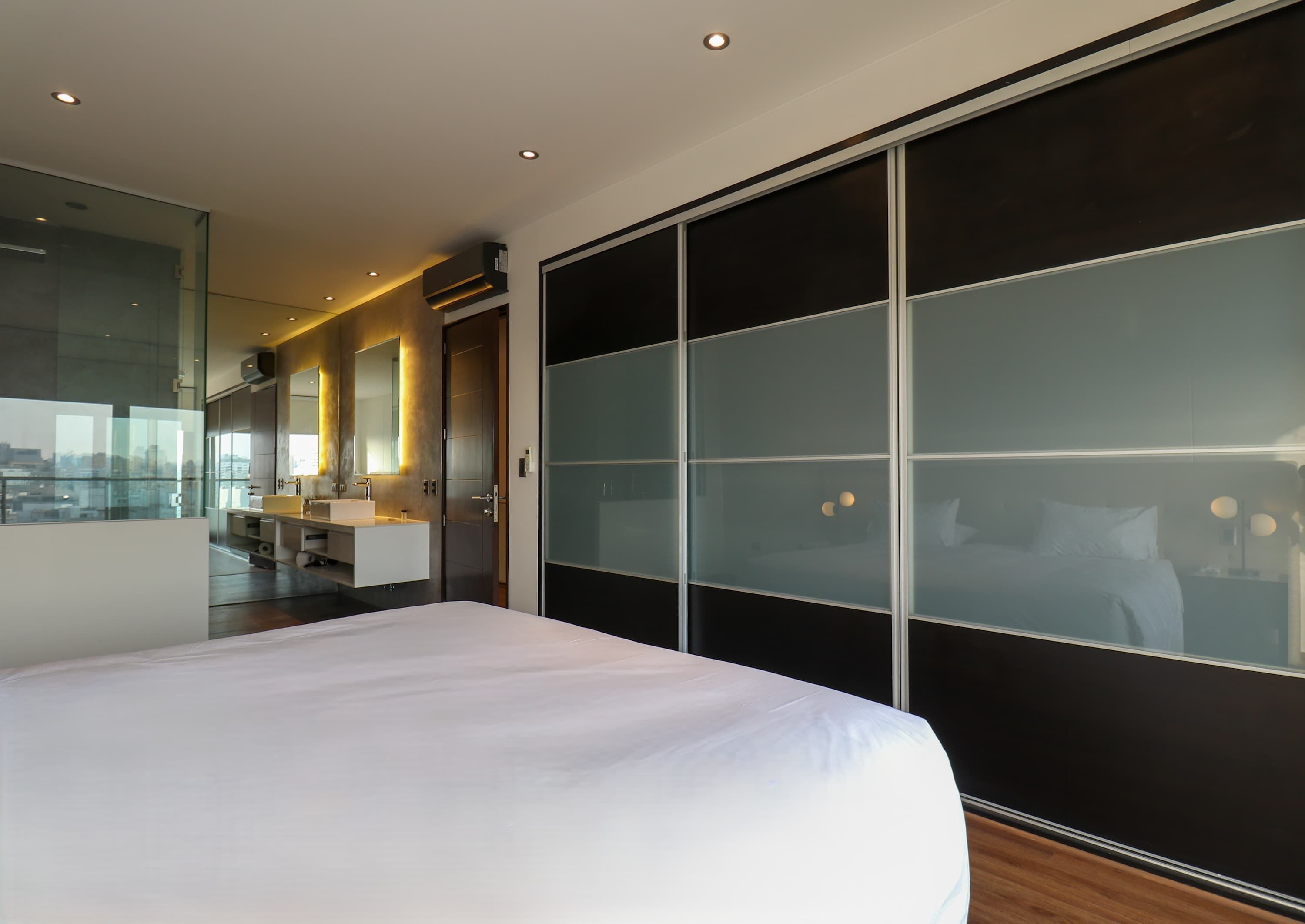 A modern hotel room with a large bed, a bathroom with a vanity, and a sliding glass door leading to a balcony.
