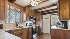 Una cocina con armarios de madera, un refrigerador de acero inoxidable, un horno empotrado y una ventana con persianas.