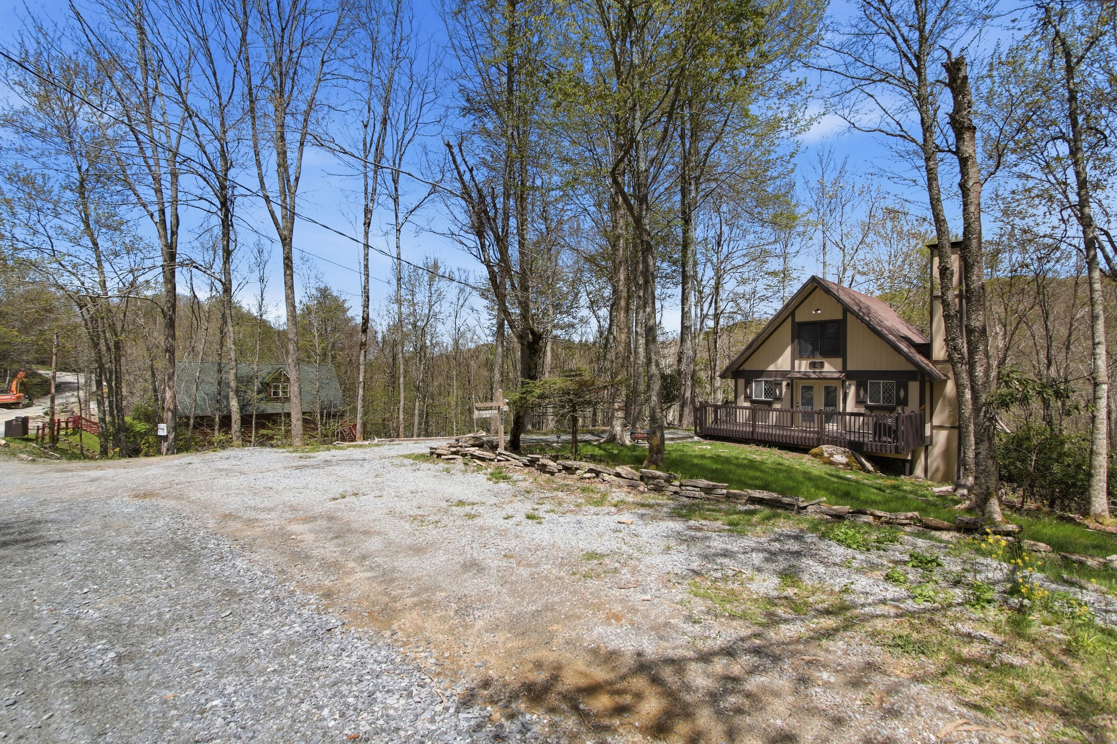 A cabin with a gravel driveway, surrounded by trees and a grassy area.