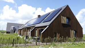 Un edificio moderno con techo inclinado, paneles solares y un jardín cercado.