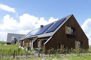 A modern building with a sloped roof, solar panels, and a fenced garden area. - Lennepserf - De Achterhoek (Veessen)