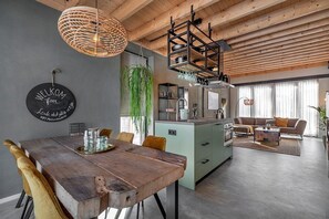 Eine moderne Küche mit einer zentralen Kochinsel, einem Essbereich mit einem Holztisch und einem Wohnzimmer mit einer Couch.