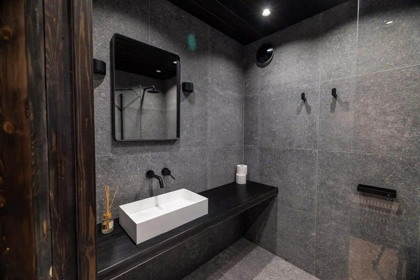 A modern bathroom with a white sink, dark countertop, and a large mirror.