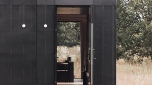 A modern, minimalist interior with a dark exterior, a wooden ceiling, and a view of a natural landscape.
