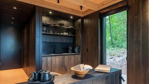 A modern kitchen with dark wood cabinets, a countertop with a kettle, a coffee maker, and a basket.