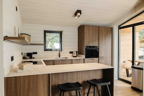 Una cocina moderna con armarios de madera, una isla central con taburetes, horno empotrado y ventana sobre el fregadero.