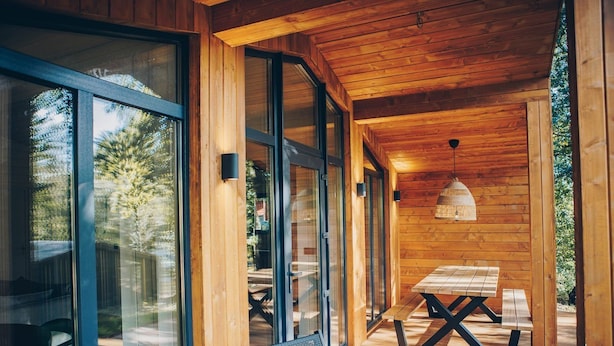 A wooden cabin with large glass doors, a picnic table, and a bench.
