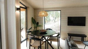 A dining area with a round table, chairs, a hanging light fixture, and a television on the wall.