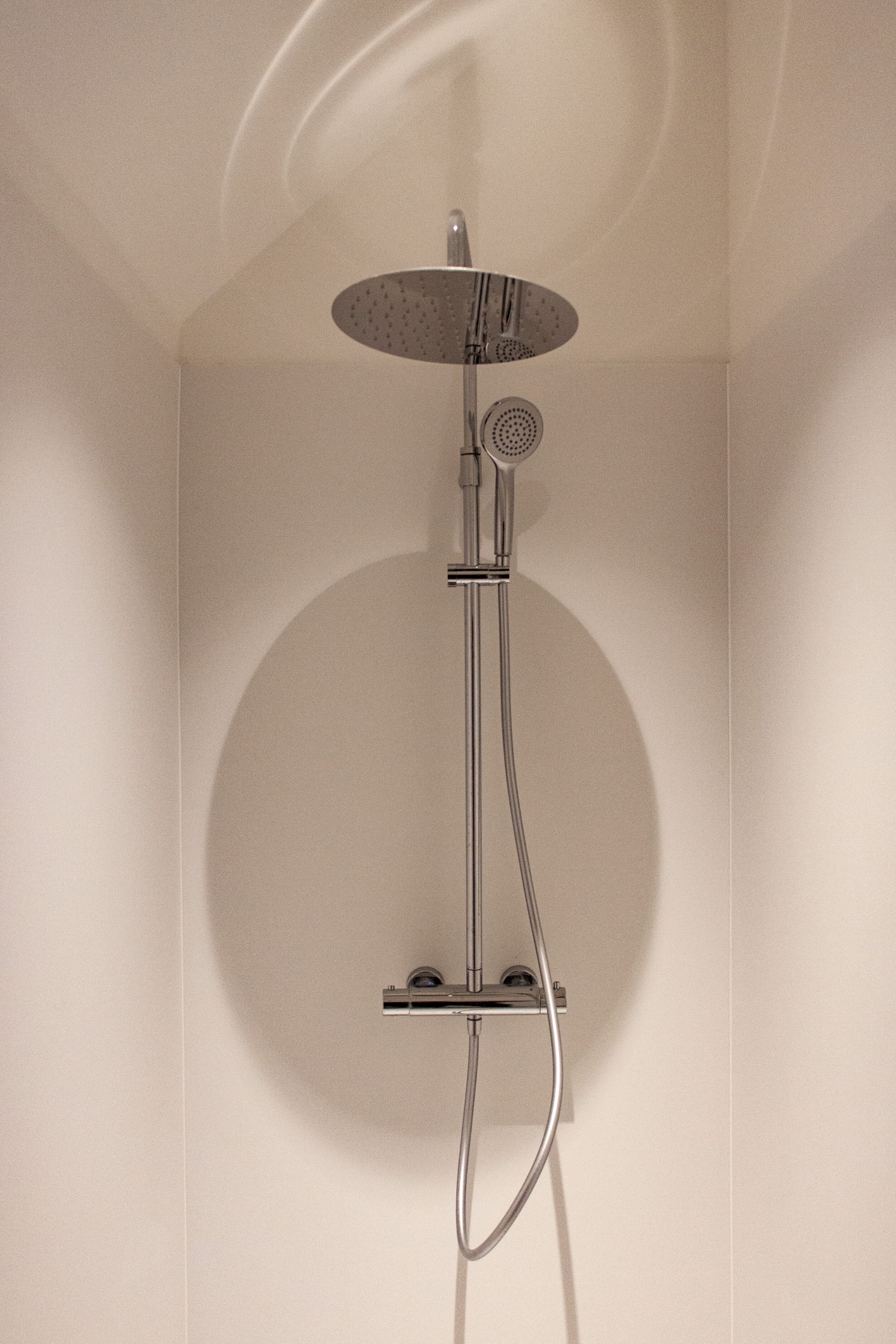 A shower with a handheld showerhead and a wall-mounted control.