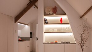 Een slaapkamer met een schuine kap, een bed met wit beddengoed, een vacht van een koe en een rood kussen.