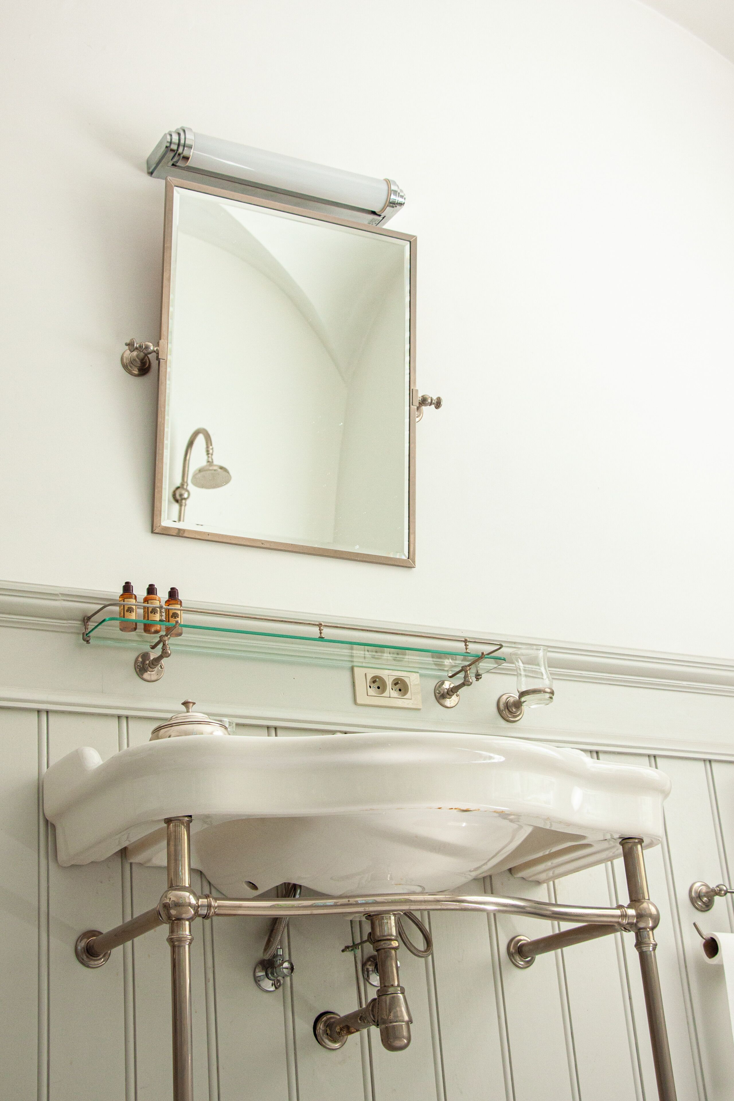 A bathroom with a white sink, a mirror, and a glass shelf above the sink.