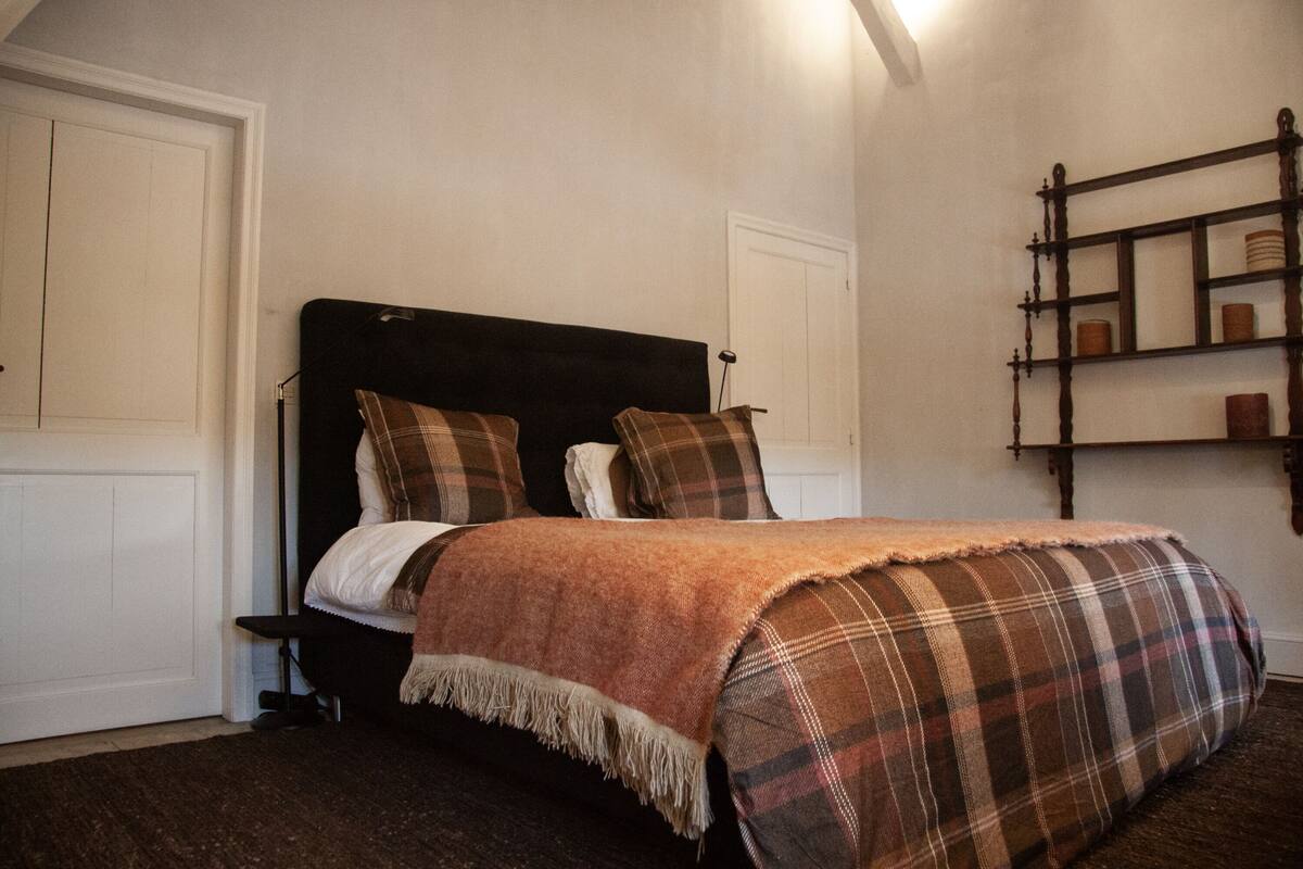 A bedroom with a bed, a headboard, a shelf with items, and a door.