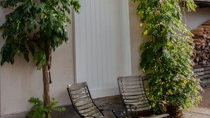 Een gebouw met een witte deur, twee metalen stoelen en klimplanten.