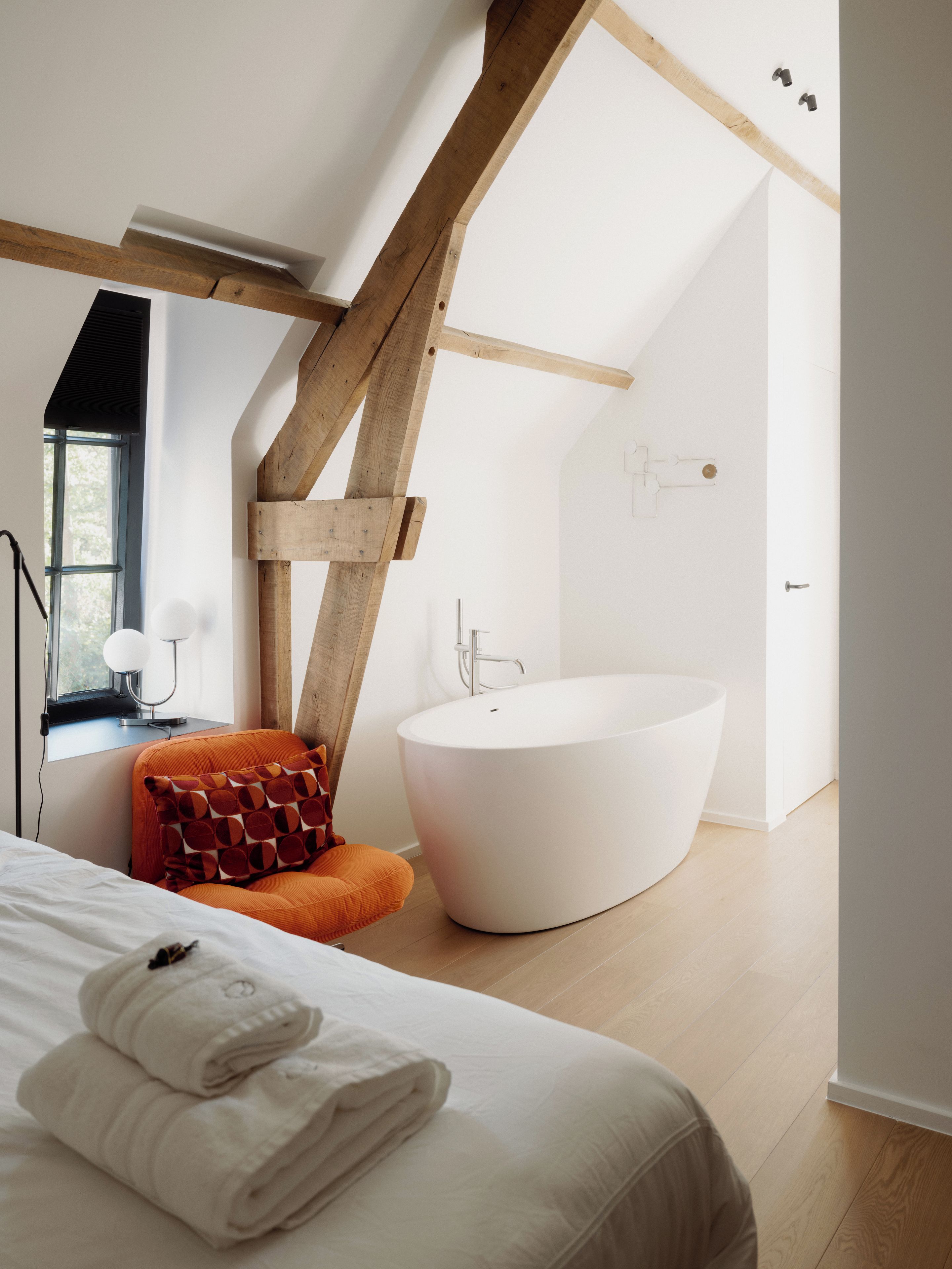 A modern bedroom with a large bed, a bathtub, and a window.