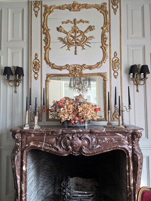 Une cheminée en marbre ornée de sculptures complexes, un miroir avec un cadre doré et des appliques murales avec des bougies.