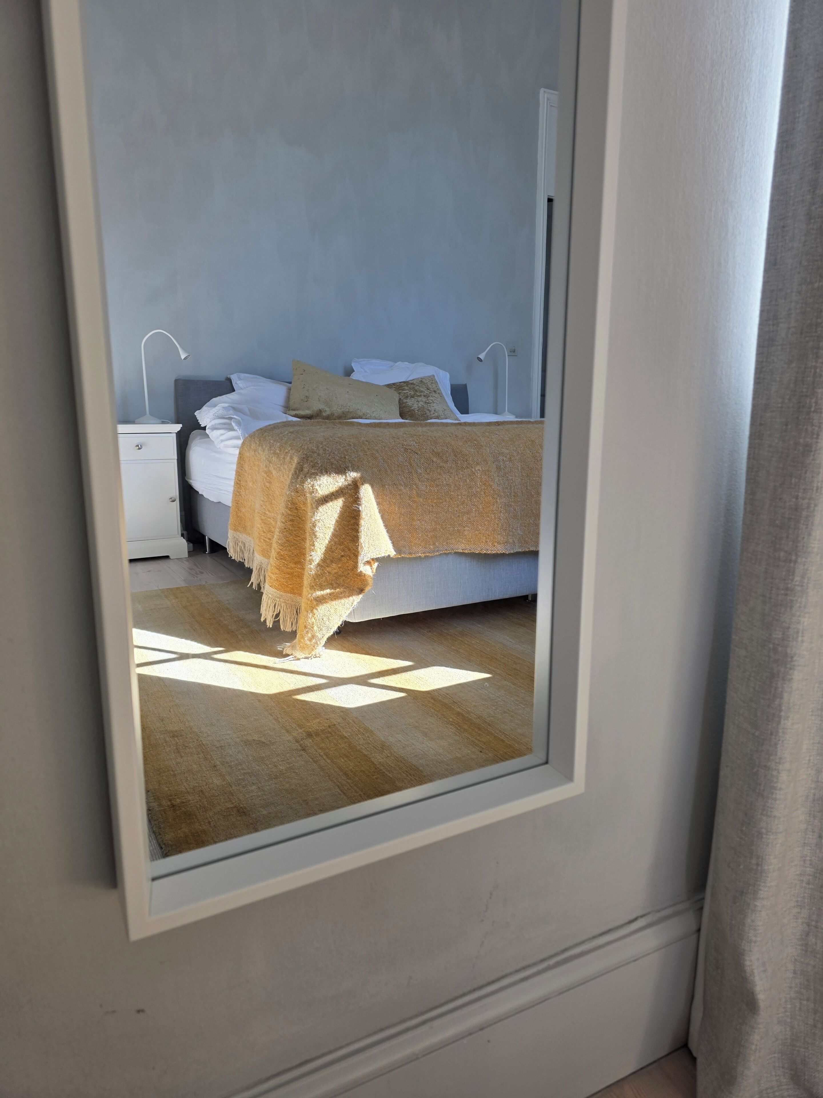 Un dormitorio con cama, mesitas de noche y un espejo que refleja la habitación.
