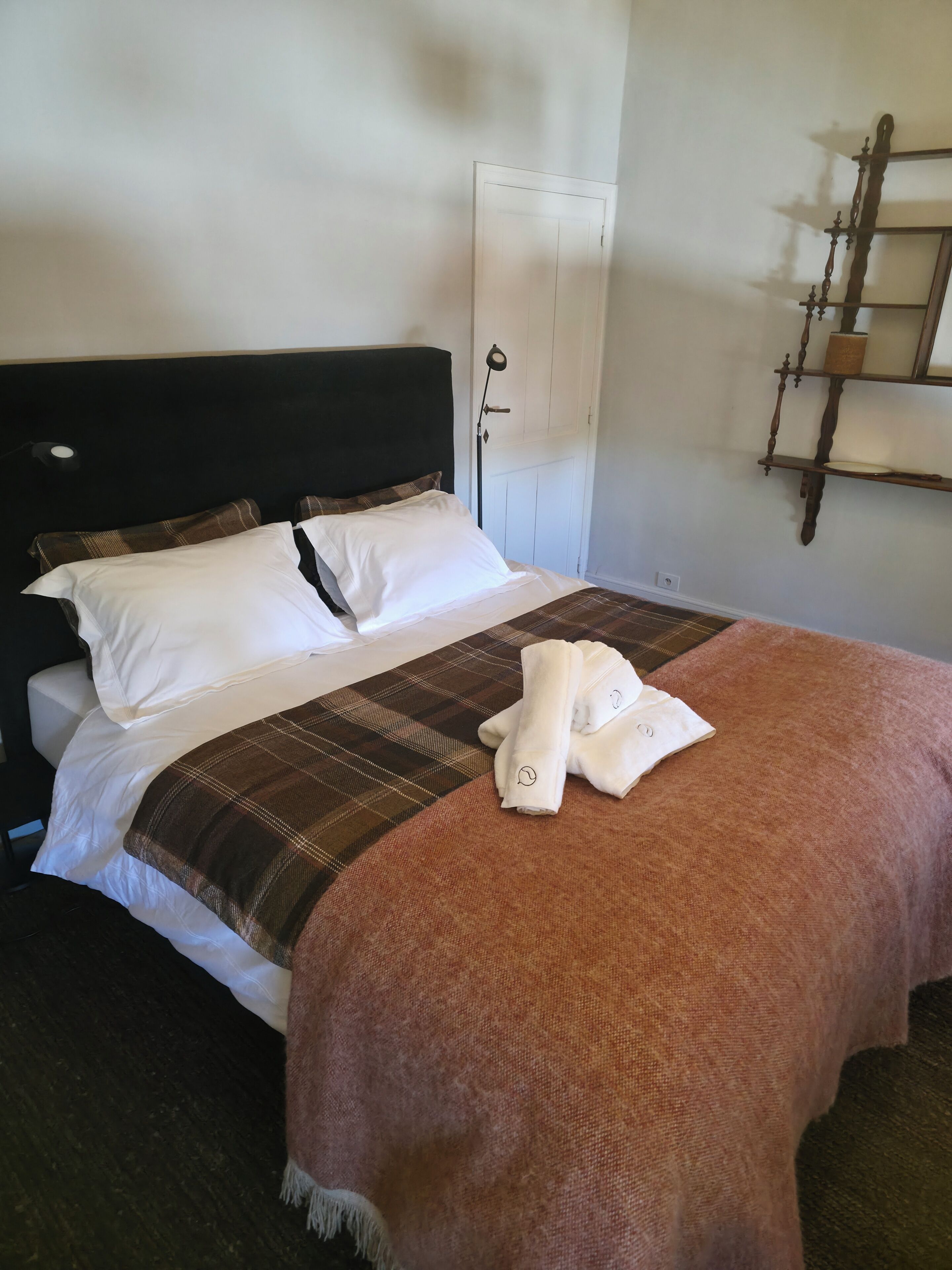 Una cama bien hecha con ropa de cama blanca y marrón, un cabecero y una lámpara de noche.