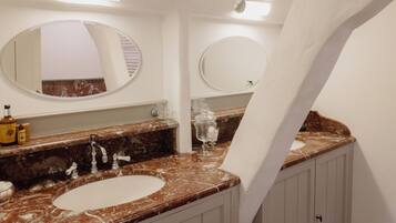 Un baño con dos lavamanos, encimeras de mármol y dos espejos redondos.