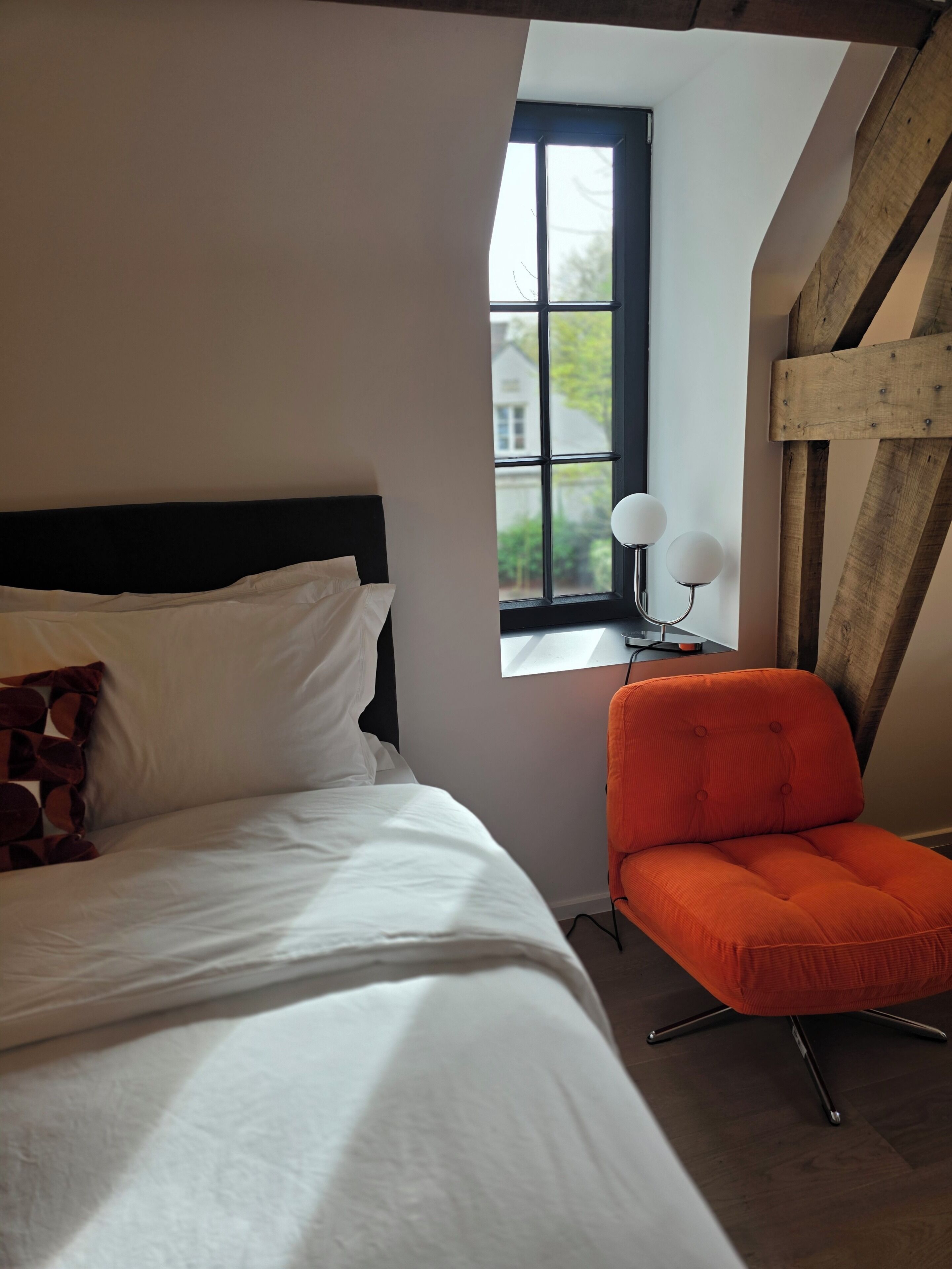 A bedroom with a bed, a window, a chair, and a lamp.
