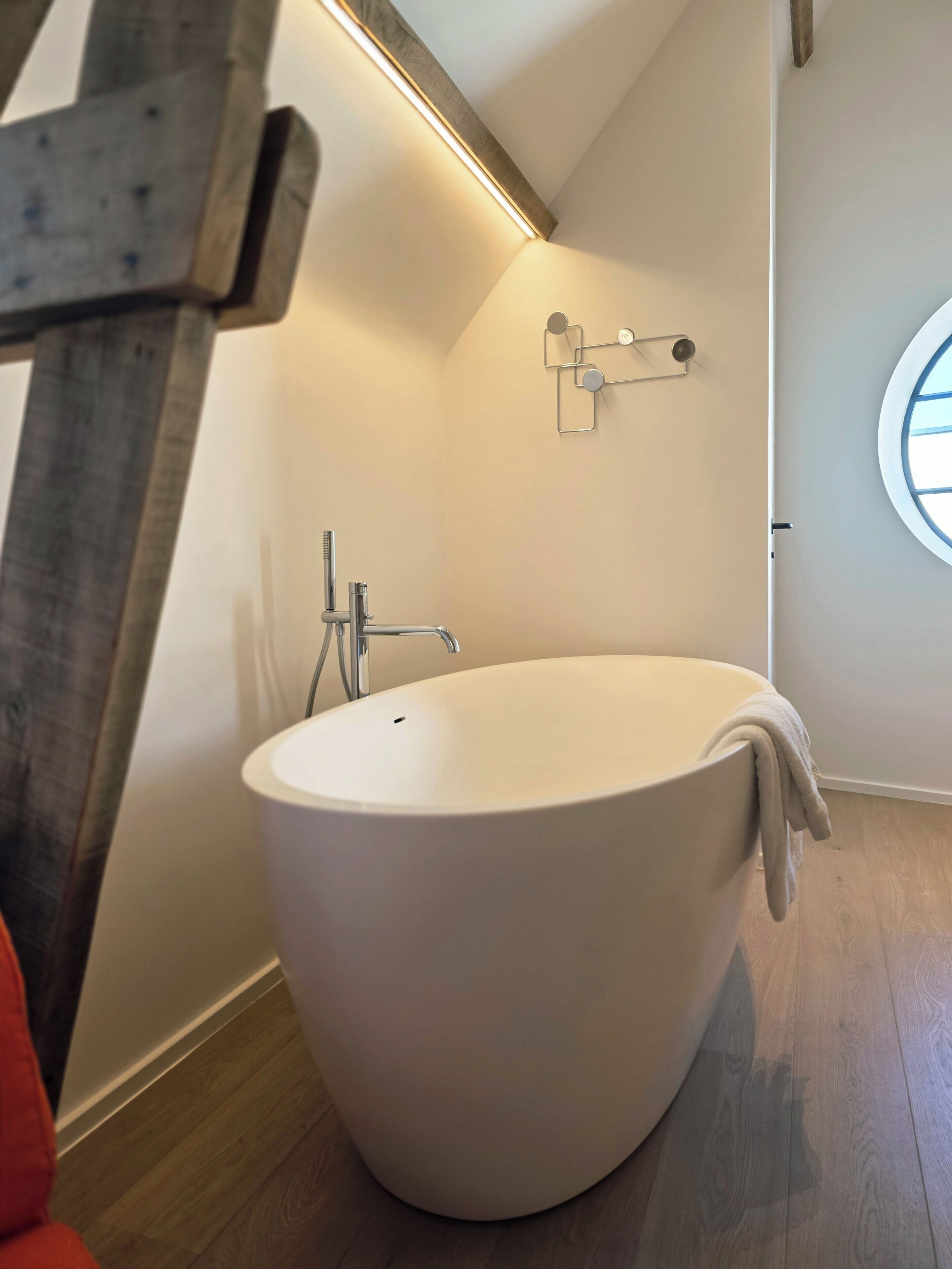 Un baño moderno con una bañera independiente, un perchero y una lámpara de pared.