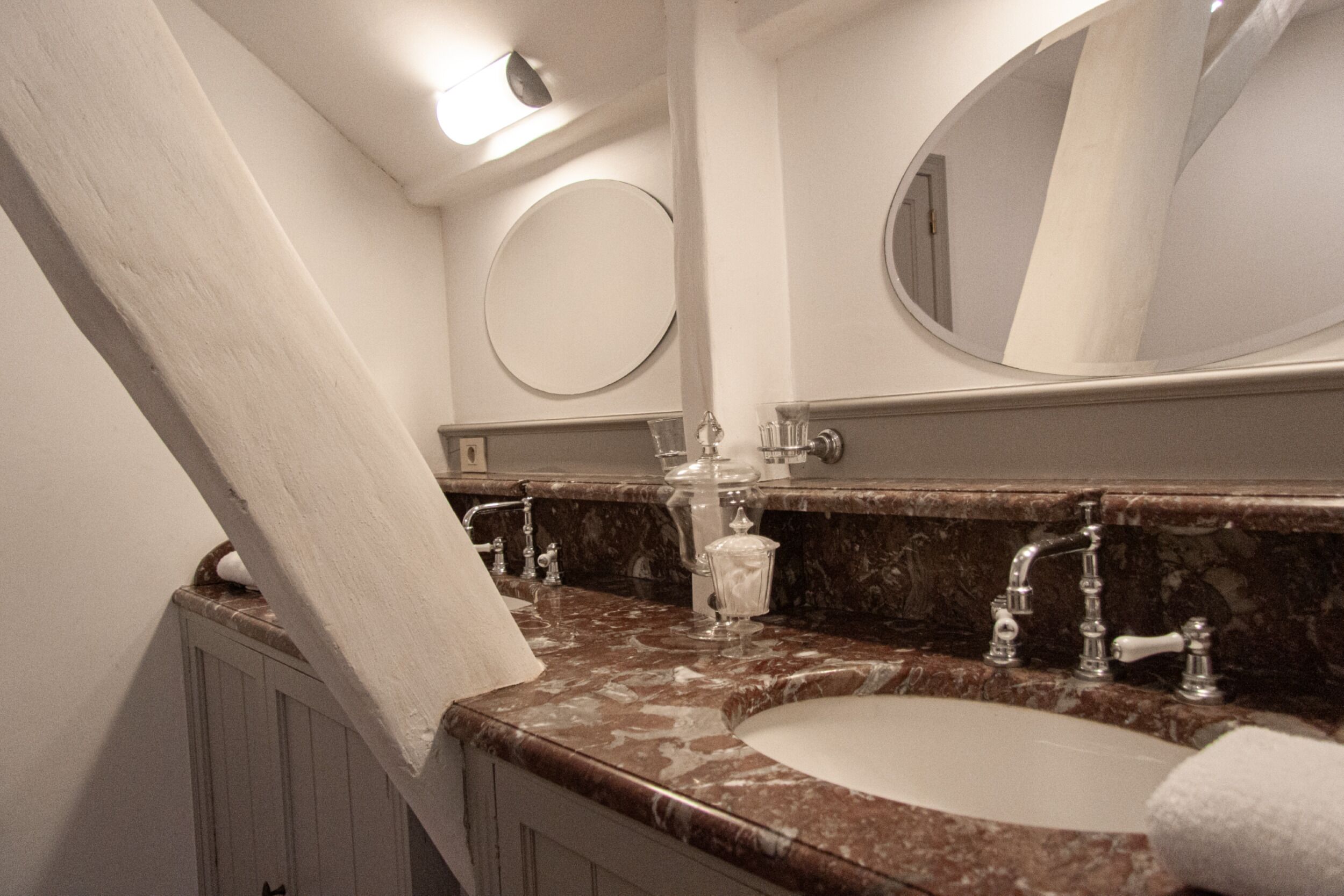Une salle de bain avec un lavabo en marbre, un miroir rond et un porte-serviettes.